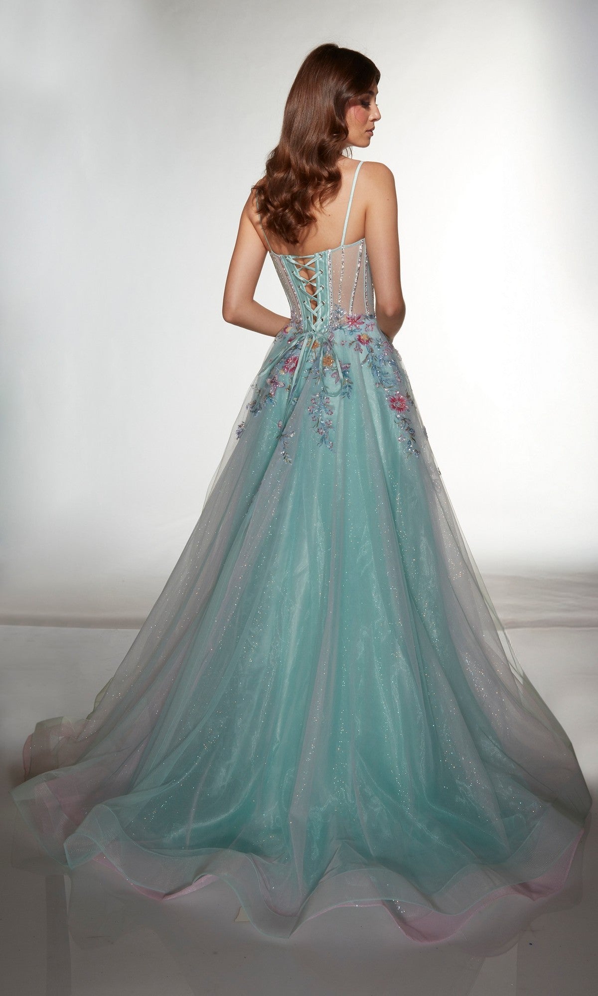 Woman models Alyce 62068, a long prom dress with a sleeveless floral corset bodice, lace-up back, and light blue floor-length sparkle tulle A-line skirt. She stands with her back to the camera against a plain background.
